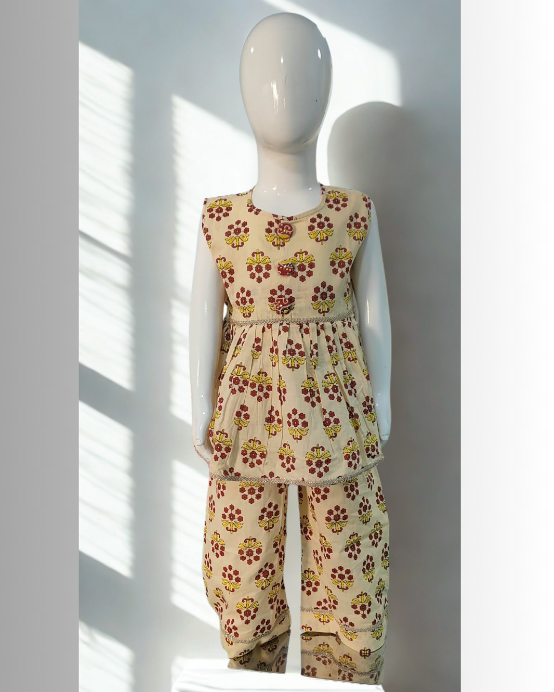 Parizaad baby girl kurti set, cream base, red-yellow floral block print, sleeveless, gathered waist, 3 buttons, gold braid, matching pants - front view