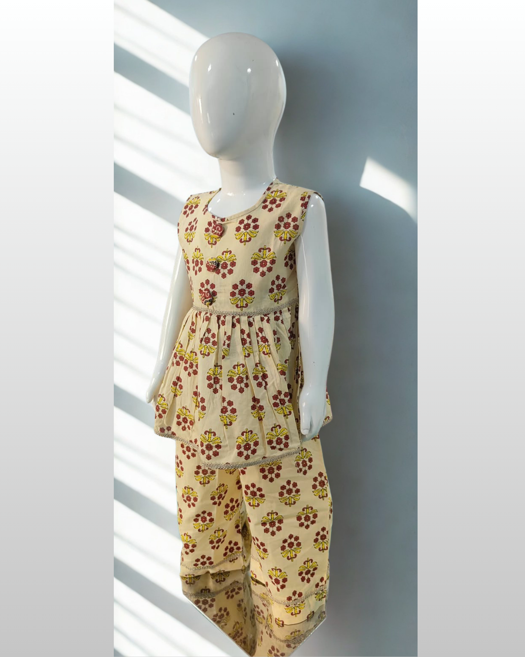 Parizaad baby girl kurti set, cream base, red-yellow floral block print, sleeveless, gathered waist, 3 buttons, gold braid, matching pants - side view