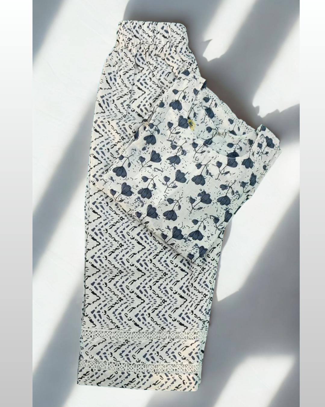 Shabana baby girl kurti set, white base, grey tulip print, three rows of cutwork lace, lace sleeve bands, grey chevron-print pants - folded